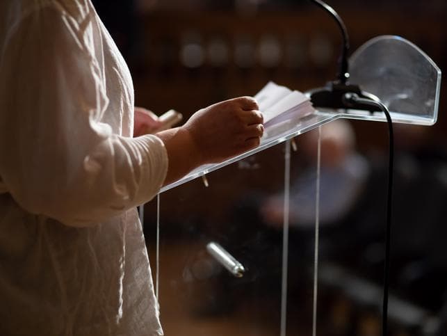 A speaker reads from notes on a podium