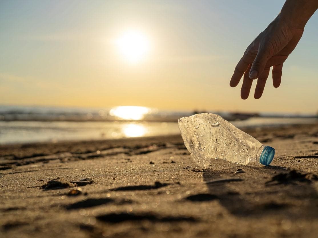 Image of someone picking up a plastic bottle from a beach