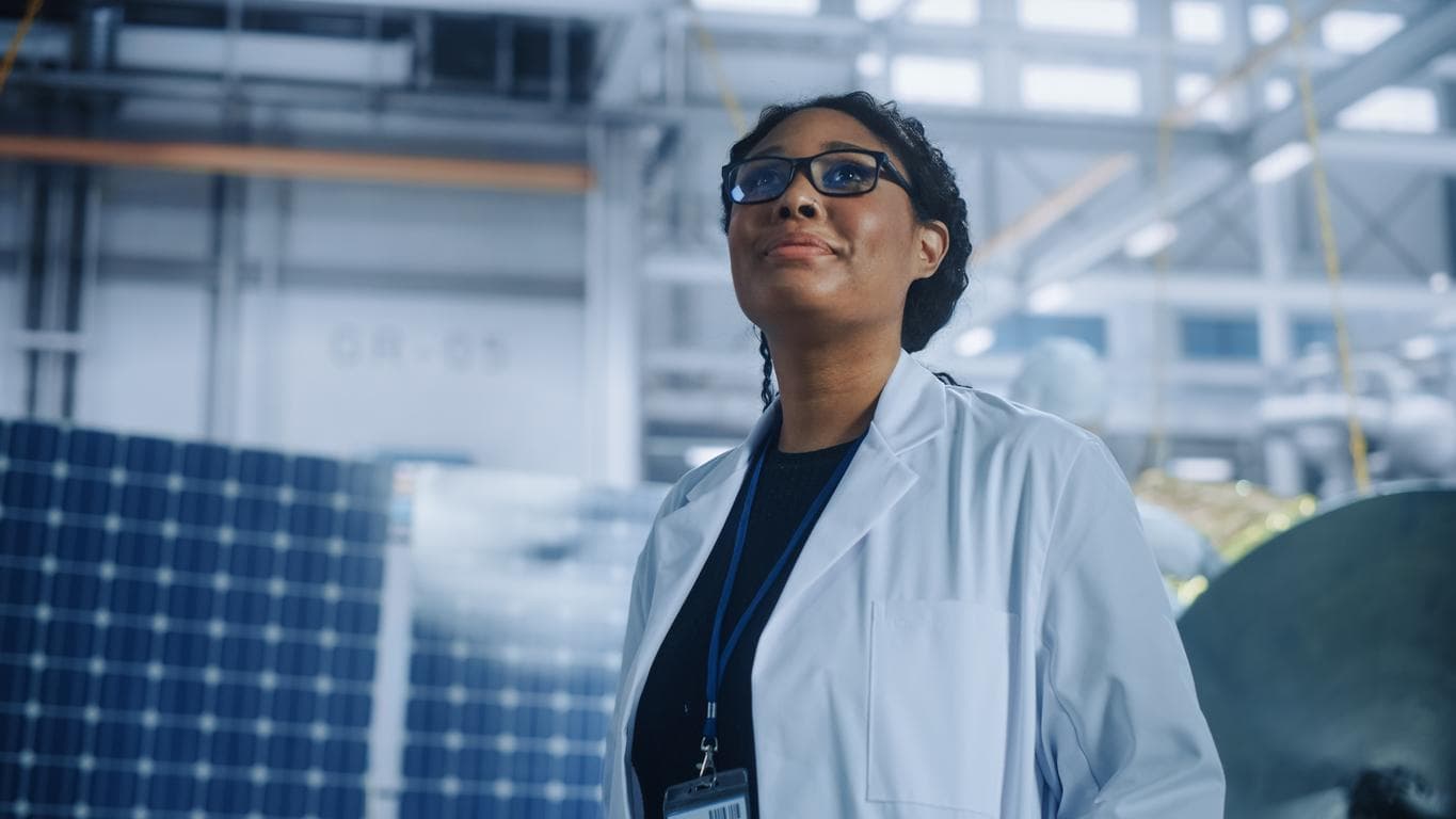 A young Black female engineer looks up in a satellite manufacturing facility