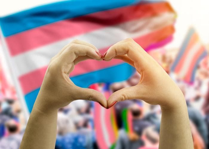 hands making a heart shape in from of a transgender flag