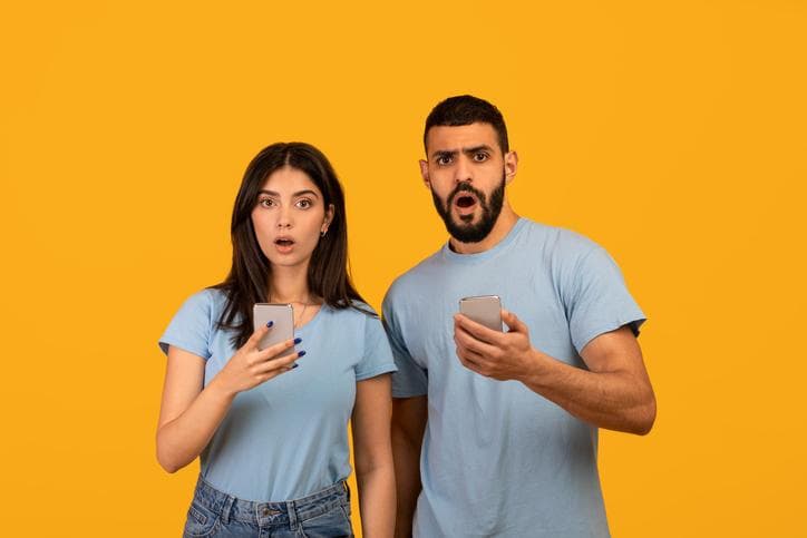 A man and a woman expressing shock at something they have seen on their phones