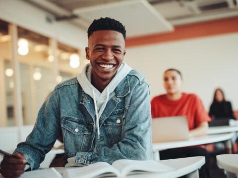 Black male student smiling at the camera from his desk