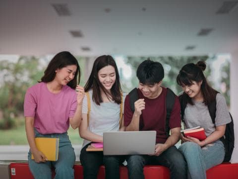 Four Asian students on a bench looking at a laptop