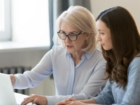 Older professional woman and young professional woman working together at laptop