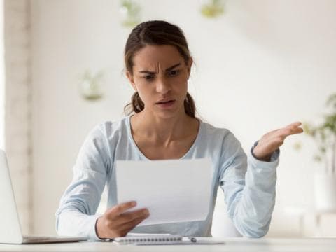 Young woman with laptop looking at paper and gesturing frustration