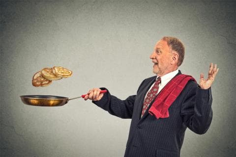 A man flipping three pancakes in a pan