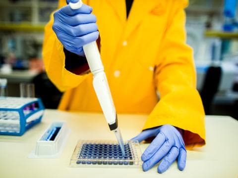 Scientist in yellow lab coat using pipette