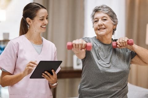 Young female health professional supervises older woman doing weights exercises