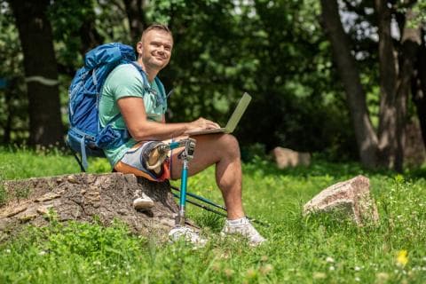A man with a prosthetic leg sitting in a forest with his laptop