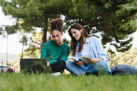 Two students sitting on the grass outside working at a laptop