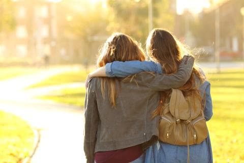 Two women walk away from the camera, their arms around each other's shoulders