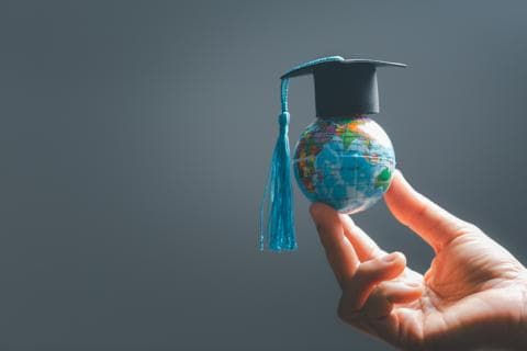 A hand holds a tiny globe wearing a mortarboard