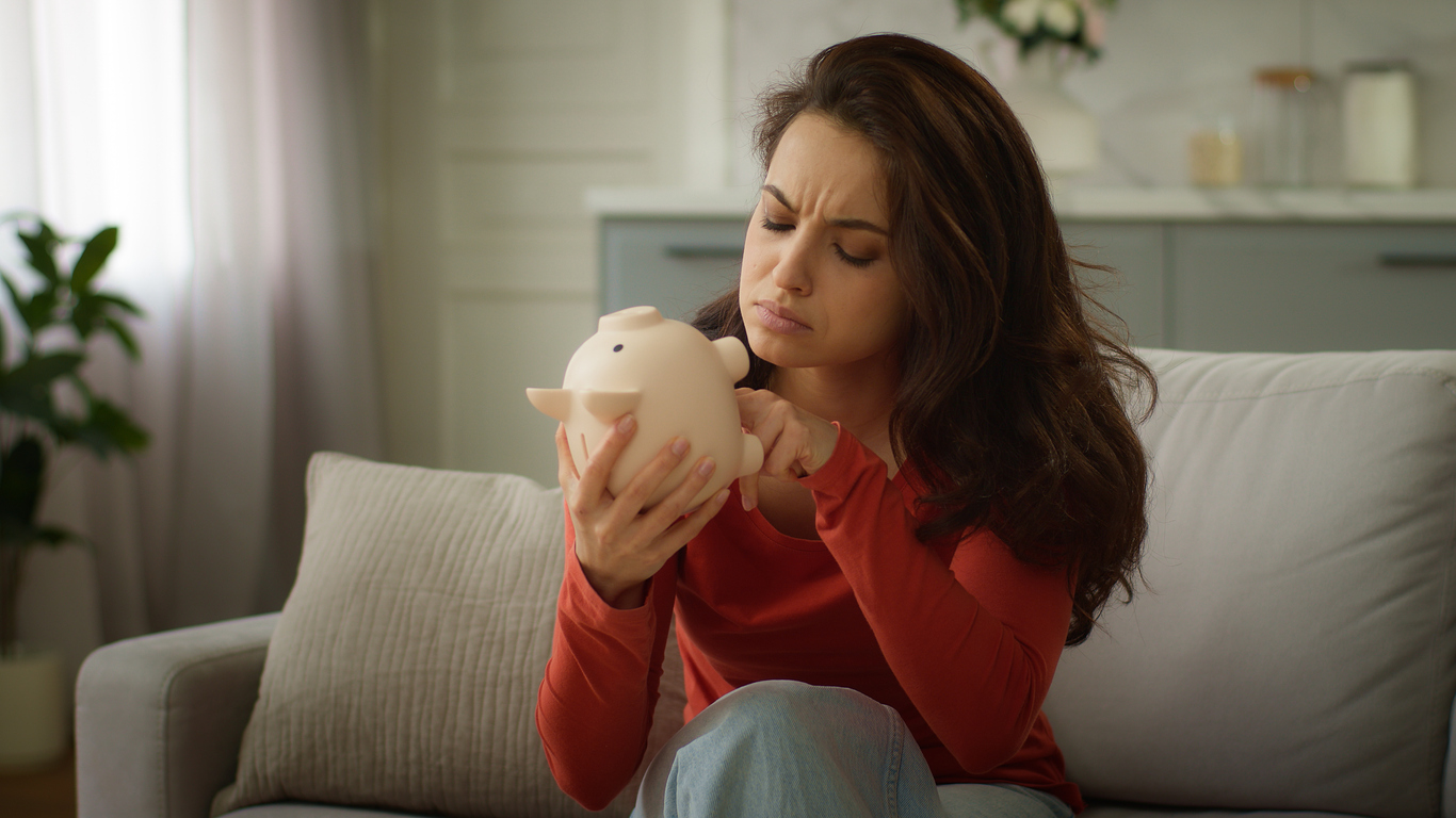 Woman tries to find coins in her empty piggy bank