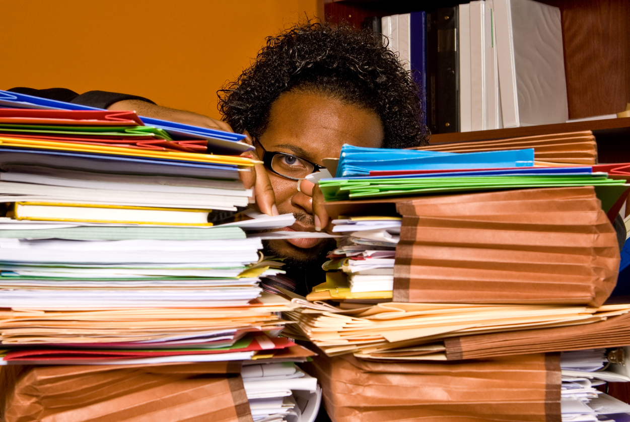 Man peering out between two huge piles of paperwork