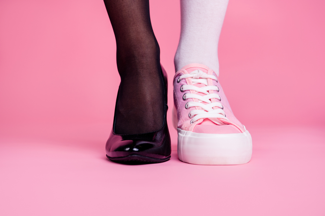 Person wearing one high-heeled shoe and one trainer
