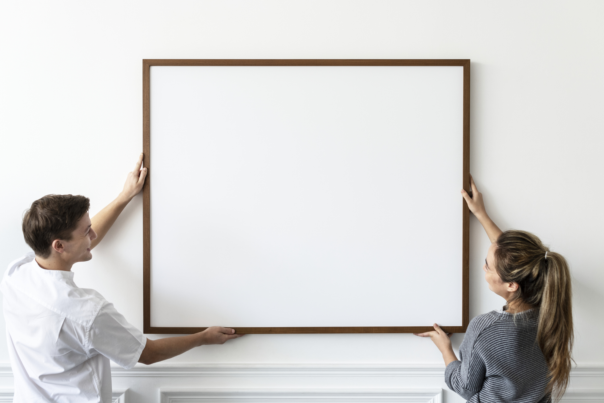 Man and woman hanging blank framed canvas on wall
