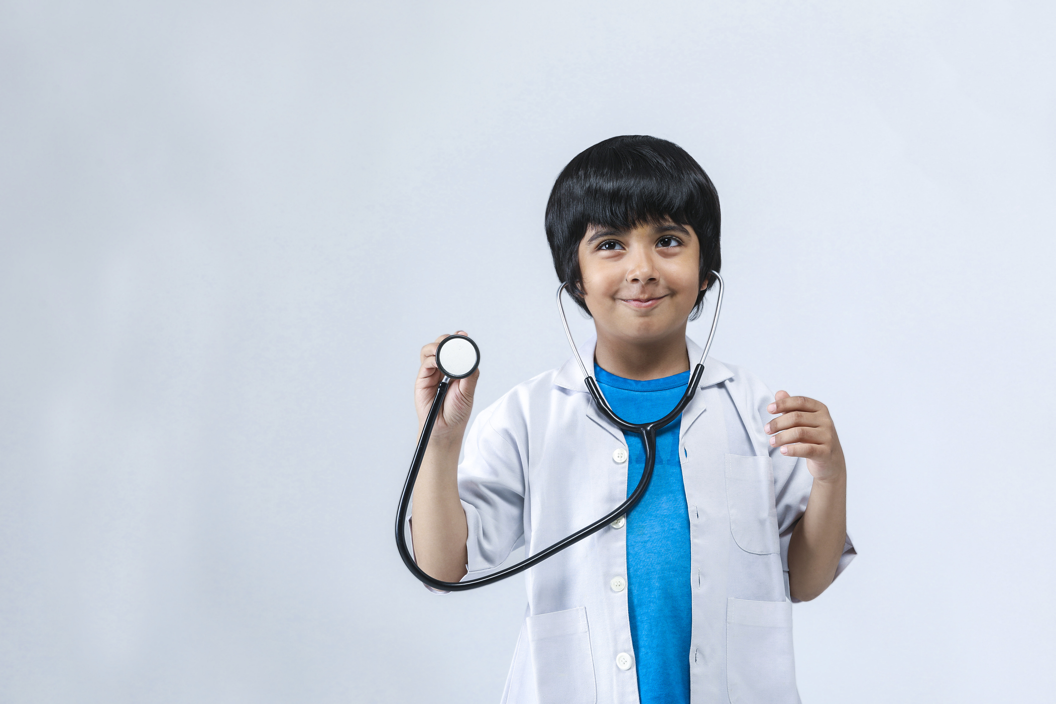 Small boy, dressed in a white coat and holding up a stethoscope