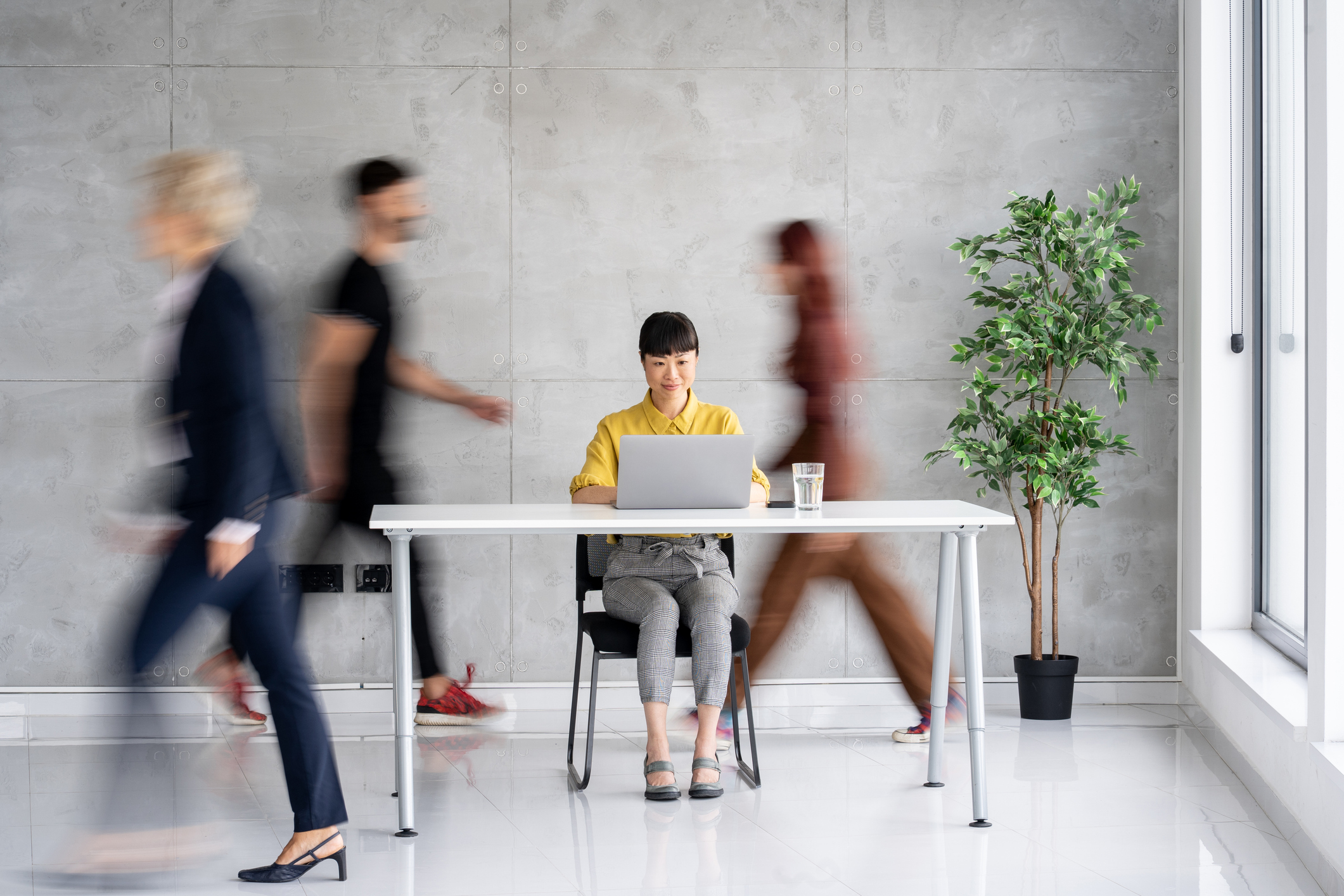 Woman sits at desk, while people rush all around her