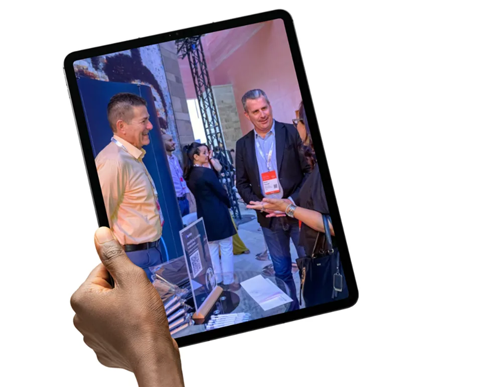 Hand holding a tablet showing delegates talking at a sector event exhibition stand