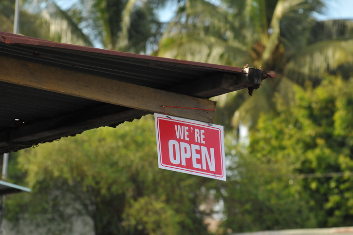 A building with plam trees behind it and a 'we're open' sign, illustrating branch campuses