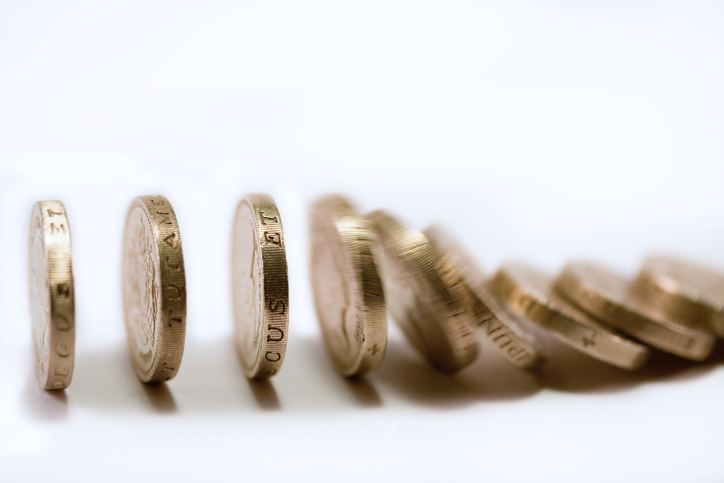 Pound coins falling like dominoes, illustrating funding precarity