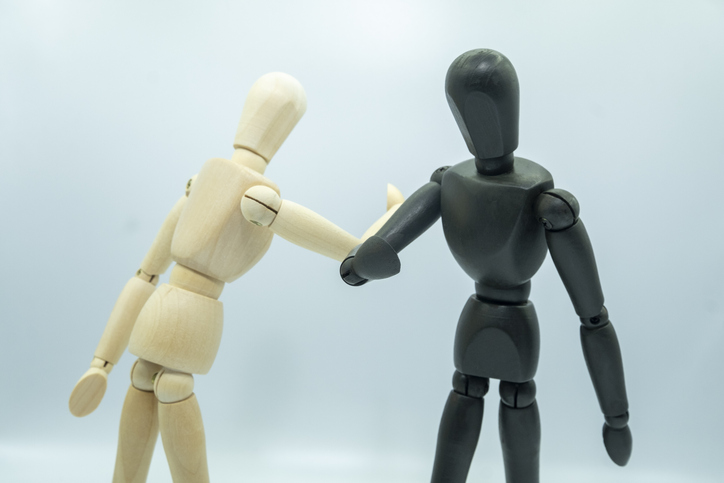 A black and a white wooden mannequin elbow bump illustrating EDI, equality diversity inclusion policy