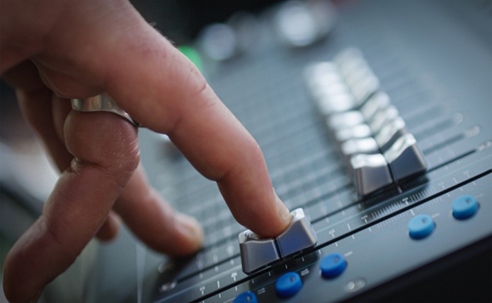 A finger slides down a fader on a mixing desk, illustrating the fading out of music scholarship