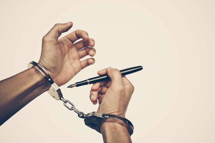 Hands handcuffed,one holding a pen, illustrating the restrictions on research caused by the GDPR