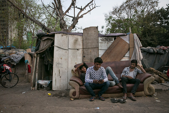 India young men sit on a sofa in a slum, illustrating graduate unemployment