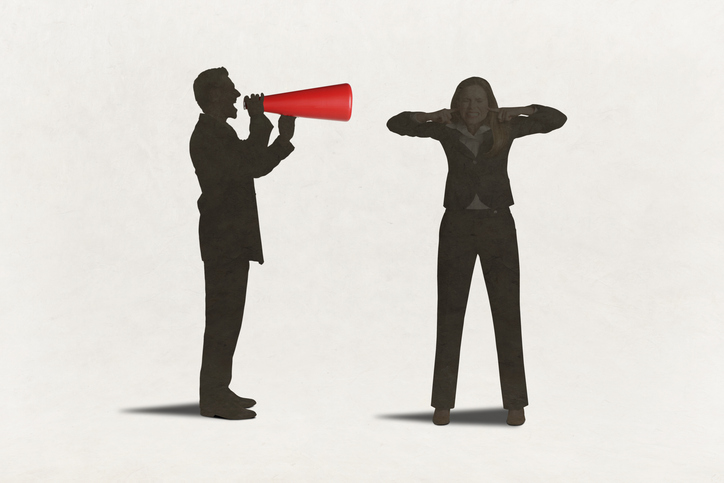 A man with a megaphone yells at a woman with her fingers in her ears