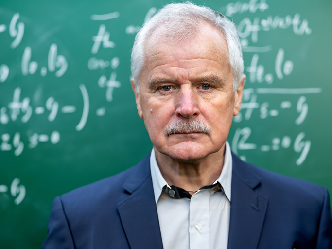 A glum old professor in front of a blackboard
