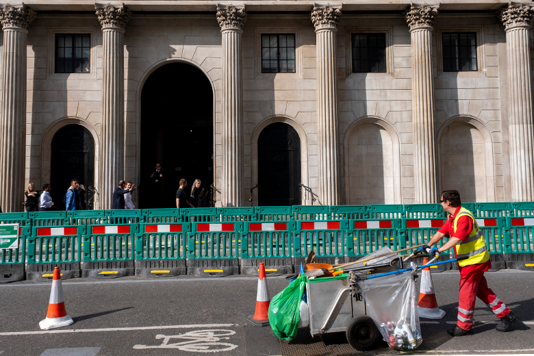 A street cleaner walks past a barrier in front of a columned building, as an illustration of how working-class people can feel excluded in higher education