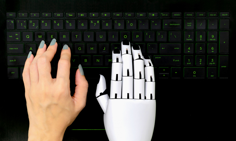 A robot and human hand on a computer keyboard, symbolising AI-assisted writing