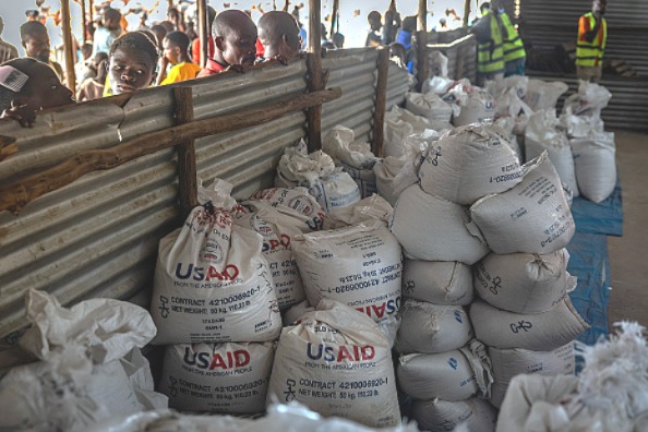 Congolese refugees look through a corrugated metal fence at the final batches of food delivered by the now-dismantled USAID in May 2025