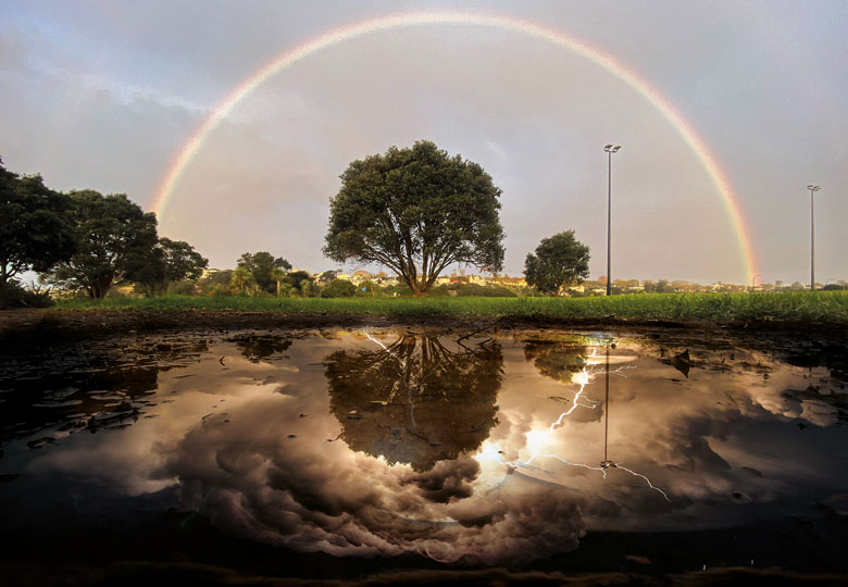 Montage: a rainbow is reflected in a puddle of water, in mono, in Auckland with lightning in the reflection to illustrate Without negative reviews, positive ones lose meaning