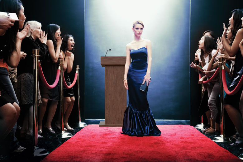 celebrity on red carpet, crowd behind barriers looking excited at seeing her.