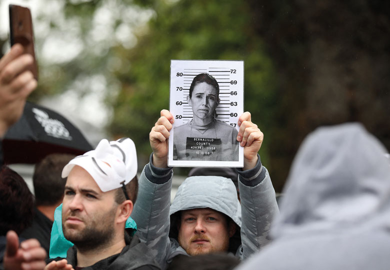 An activist holds a picture of New Zealand Prime Minister Jacinda Ardern stylised as a police mugshot to illustrate Female leaders need support – not the abuse they currently endure
