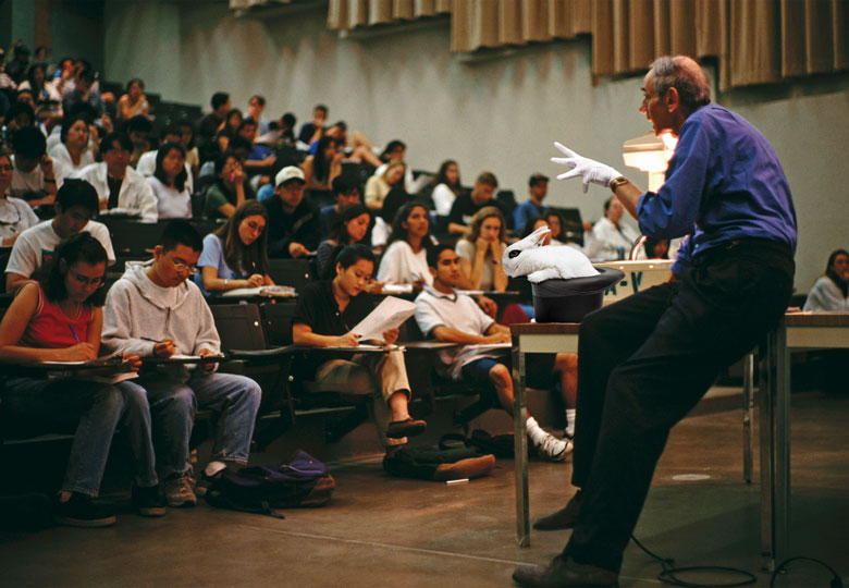 Montage of a professor giving a lecture with a magic glove, hat and white rabbit to illustrate If live lectures die, how will the true magic of shared endeavour be conjured up?