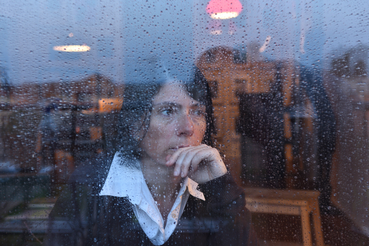 A woman looks out of a rain-splashed window, illustrating genderwashing