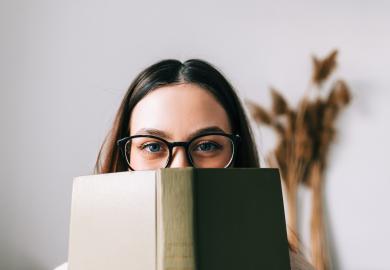 Student peers over the top of a book