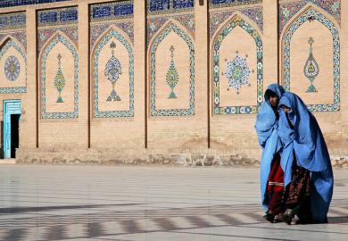 Two women in blue burqas walk at the front of a mosque with a door open, symbolising an open university