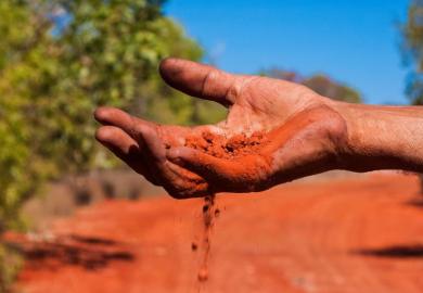 Red Australian earth slips through an Indigenous Australian’s fingers