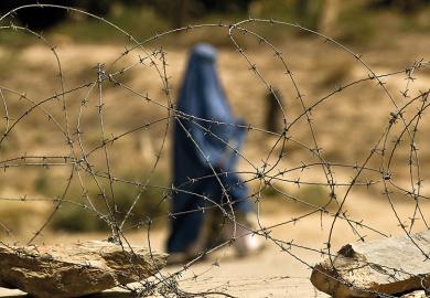 A covered Muslim woman walks behind some barbed wire