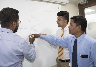 Indian business academics discuss a theory on a whiteboard