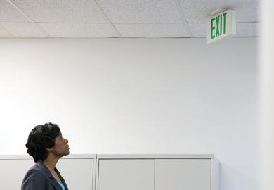Businesswoman looking up at office 'Exit' sign