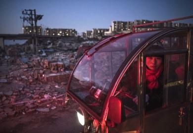 A Chinese woman drives past collapsed buildings