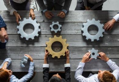 People hold unconnected cogwheels, one of which is gold