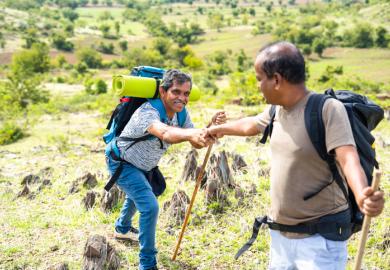 An Indian man helps another one up a hill, symbolising collaboration to improve