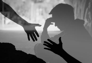 Hands reach for each other in front of a depressed man, symbolising suicide prevention