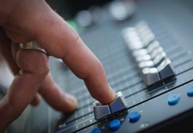 A finger slides down a fader on a mixing desk, illustrating the fading out of music scholarship